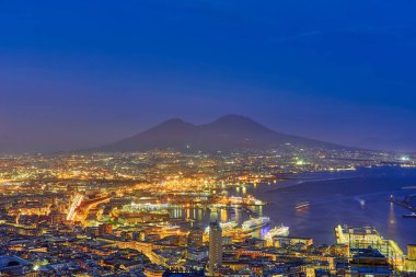 Vomero bölgesinden Napoli 'nin gece görüşü. Castel Sant 'elmo ön planda, arka planda şehrin limanı ve Ovo kalesi. Evler ve binalar var..