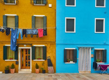 Kuzey İtalya 'daki Burano adasındaki güzel renkli ev cephesi. Yarı turuncu, yarı mavi, sarı kapılı ve içinde bitkiler olan iki pencereli ev duvarı.