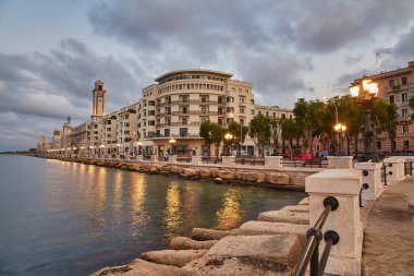 Bari, İtalya 'da deniz önü ve gezinti güvertesinde boş bank ve lamba direkleri. Romantik, sakin, rahatlatıcı bir akşam. Güneş batıyor.