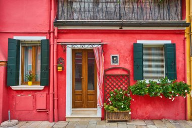 Evin kırmızı cephesinde çiçekli kapı ve pencereler. Burano Adası, Venedik, İtalya 'da renkli mimari.