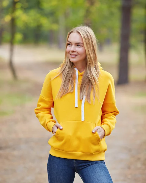 stock image Beautiful young blonde woman in yellow hoodie walks in the park. Attractive female spending active time in the park. Portrait of a joyful young woman enjoying in autumn park. Relax in nature.