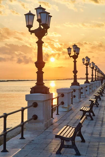 Empty benches and lamp posts at seafront and promenade in Bari, Italy. Romantic, calm, relaxing evening in city. Sun is setting