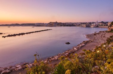 Güzel turuncu gün batımı ya da İtalya, Otranto Limanı üzerinde gün doğumu. Yumuşak bulutlar, sakin okyanus ve arkadan aydınlanan gökyüzü ve yat ve balıkçılarla dolu marina. Yatay çerçevedeki turistik manzara
