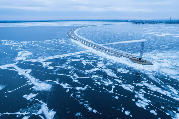 Breakwater leading into Baltic sea at winter. Sea covered in fog and ice blocks. Beautiful lighthouse at sunrise.