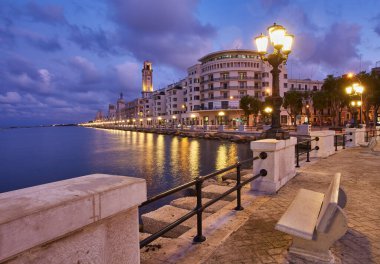 Bari, İtalya 'da deniz önü ve gezinti güvertesinde boş bank ve lamba direkleri. Romantik, sakin, rahatlatıcı bir akşam. Güneş batıyor.