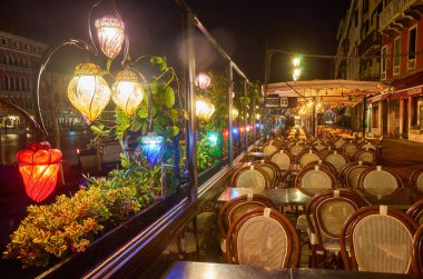 Venedik, İtalya 'da köprü ve restoran masaları olan bir cadde. Venedik 'in mimarisi ve simgesi. Venedik 'in gece sıcacık şehri.