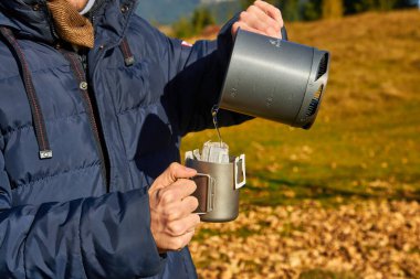 Turist, güzel sonbahar dağlarının ve doğanın arka planında damlayan kahve yapar.