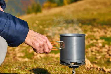 Bir adamın eli, dağların arka planında yemek yemek için bir kap tutuyor, bir fast food sistemi, güvenli bir gaz ocağı, yürüyüş ekipmanları, yürüyüş aletleri. Yüksek kalite fotoğraf