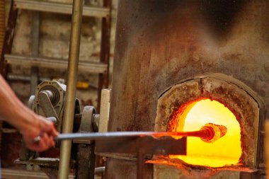 Murano cam üfleme fabrikası. Hava üfleyici çok güzel bir cam parçası oluşturuyor: camı işlenebilir hale getirmek için fırına demir çubuk ve cam nesne iliştirin. Venedik, İtalya