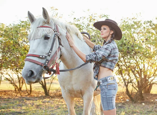 美丽的黑发女人长头发和马 一个戴着牛仔帽的女孩和她的马的肖像 美丽的女孩在农场里和一匹马交流和玩乐 — 图库照片