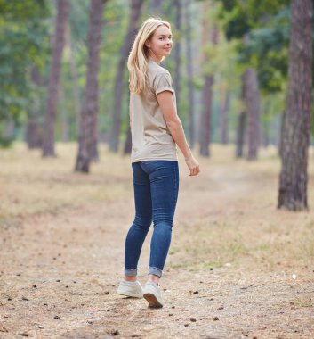 Çam ormanında poz veren doğal makyajlı sarışın kadın. Güzel mavi gözlü, bej tişörtlü beyaz kadın yaz tatilinin tadını çıkarıyor. Vahşi yaşam ve insanlar kavramı.