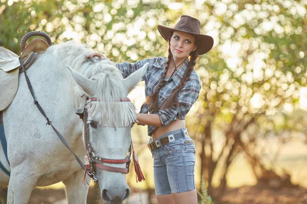 美丽的黑发女人长头发和马 一个戴着牛仔帽的女孩和她的马的肖像 美丽的女孩在农场里和一匹马交流和玩乐 — 图库照片