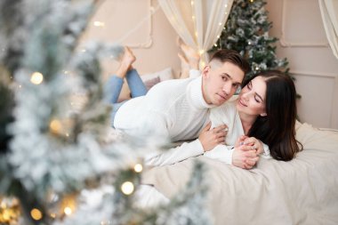Birbirine aşık genç bir çift Noel ağacının yanında duruyor ve sarılıyor.