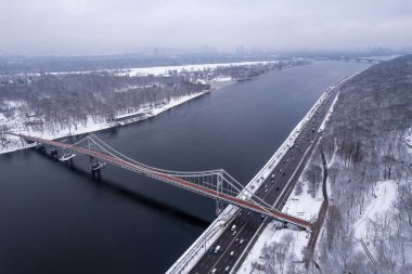 Hava aracı görüntüsü. Kiev 'deki donmuş Dinyeper Nehri üzerindeki yaya köprüsü. Bulutlu, dondurucu bir kış sabahı, buzda soğuk bir desen..