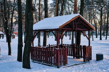 Güneşli bir günde, kış parkında eski ahşap bir çardak. Parktaki ahşap çardak. Parkta karla kaplı ahşap bir çardak..
