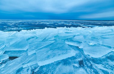 Çarpıcı bir kış manzarası, kristal kadar berrak mavi bir buz örtüsüyle göl kıyılarını nazikçe kaplayan donmuş doğal güzelliğin çarpıcı bir görüntüsüyle.