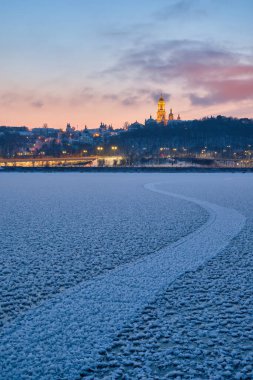 Güneş bir kış akşamı batarken Kyiv 'deki Dnipro Nehri, ikonik Kyiv Pechersk Lavra' nın nefes kesici manzarasını sunan donmuş, parıldayan bir başyapıta dönüşür.