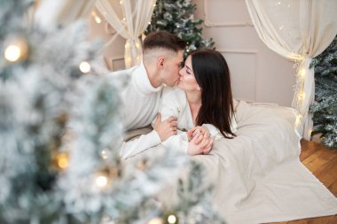 Birbirine aşık genç bir çift Noel ağacının yanında duruyor ve sarılıyor.