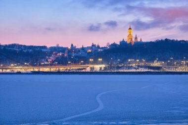 Güneş bir kış akşamı batarken Kyiv 'deki Dnipro Nehri, ikonik Kyiv Pechersk Lavra' nın nefes kesici manzarasını sunan donmuş, parıldayan bir başyapıta dönüşür.