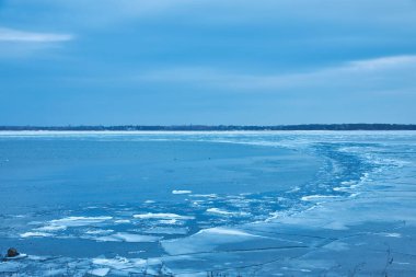 Çarpıcı bir kış manzarası, kristal kadar berrak mavi bir buz örtüsüyle göl kıyılarını nazikçe kaplayan donmuş doğal güzelliğin çarpıcı bir görüntüsüyle.