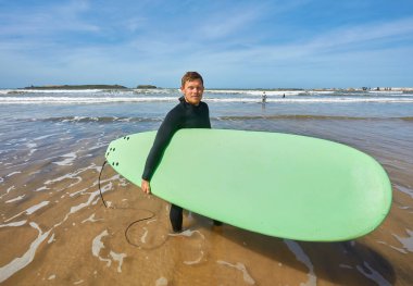 Genç bir sörfçü sörf tahtası ile Essaouira 'daki okyanus kıyısında poz vererek, Atlantik' in pitoresk zeminine karşı sörf kültürünün özünü yakalıyor.