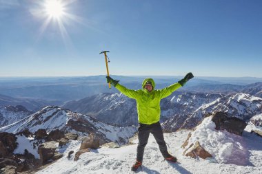 Fas 'ın Toubkal Dağı' nın zirvesinde zafer kazanan bir turist, yükselişi el kaldırarak ve buz baltasıyla kutluyor..