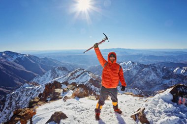 Turuncu ceketli profesyonel rehber, kolları havada bir kayanın tepesinde tırmanışın bir sonraki zaferinden memnun.