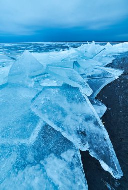 Çarpıcı bir kış manzarası, kristal kadar berrak mavi bir buz örtüsüyle göl kıyılarını nazikçe kaplayan donmuş doğal güzelliğin çarpıcı bir görüntüsüyle.
