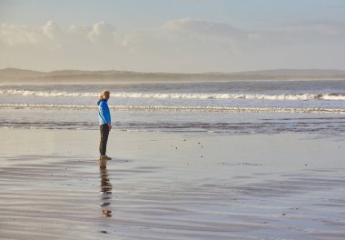 Genç bir kadın, Essaouira 'nın okyanusu boyunca uzanan ve ritmik dalgaların canlandırıcı koşusu için rahatlatıcı bir zemin oluşturduğu bir deniz kıyısının sakinliğini kucaklıyor.
