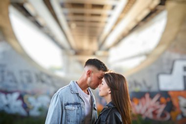 Arka planda büyük bir köprüyle dışarıda poz veren genç ve şık bir çift..