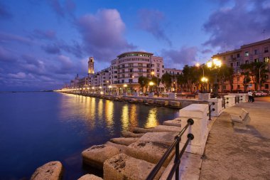 Bari, İtalya 'da deniz önü ve gezinti güvertesinde boş bank ve lamba direkleri. Romantik, sakin, rahatlatıcı bir akşam. Güneş batıyor.