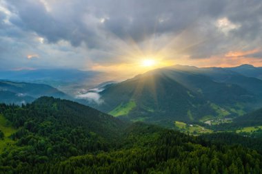 Yazın gün doğumunda bulutların içinde dağlar. Siste yeşil ağaçlar olan dağ zirvesinin havadan görünüşü. Yüksek kayalar, orman ve gökyüzü olan güzel bir manzara. Dağ vadisinin alçak bulutlu insansız hava aracı manzarası