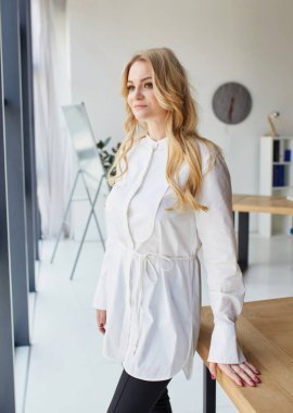 Beautiful business woman blonde in a blouse and trousers smiles and looks out the window. Vertical photo