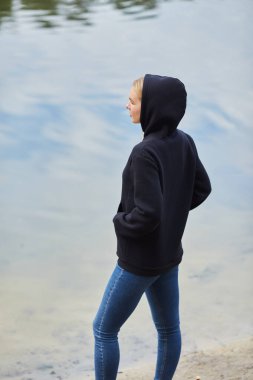 Siyah kapüşonlu neşeli mavi gözlü sarışın kız, park geçmişine karşı gülümsüyor. Dışarıda poz veren şık elbiseli çekici bir sarışın. Doğada rahatla..