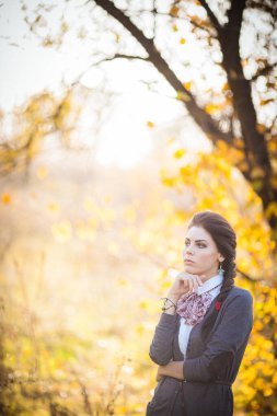 In the enchanting autumn forest, a brunette girl stands, captivated by the serene beauty surrounding her. The golden sunlight filters through the colorful canopy, casting a warm glow on her. clipart