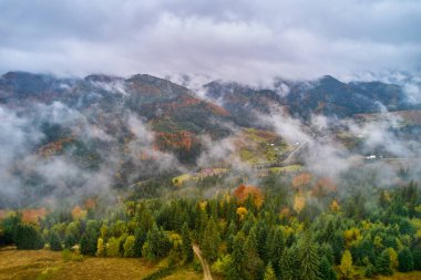 Yazın gün doğumunda bulutların içinde dağlar. Siste yeşil ağaçlar olan dağ zirvesinin havadan görünüşü. Yüksek kayalar, orman ve gökyüzü olan güzel bir manzara. Dağ vadisinin alçak bulutlu insansız hava aracı manzarası