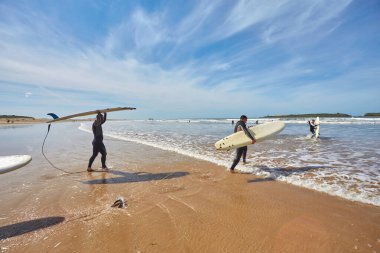 A vibrant band of young surfers dashes into the ocean, boards in tow, embracing the thrill of meeting the waves head-on. Each stride echoes the enthusiasm of a surfing adventure unfolding clipart