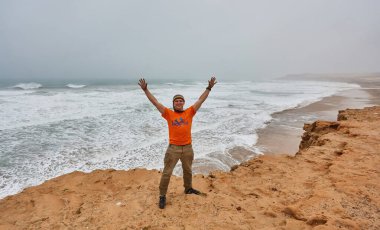 Tourists on the shores of the Atlantic Ocean in Morocco. Rainy weather. People are happy to meet the ocean for the first time. clipart