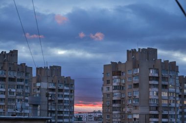 Gün batımında dramatik bulutlu bir gökyüzü tarafından çerçevelenmiş apartmanlar. Ufuktaki kara bulutlar ve pembe ipuçları kasvetli, kentsel bir atmosfer yaratır..