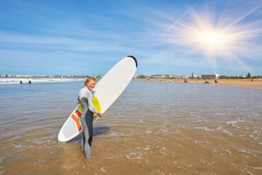 A young female surfer strikes a pose with her board on Essaouira's oceanfront, embodying a graceful fusion of surf culture and coastal charm. clipart