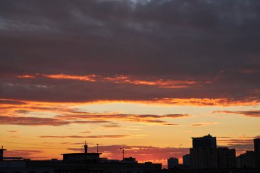 A city skyline at dusk with a gradient sky transitioning from warm orange to deep blue. The silhouettes of buildings and cranes are visible against the glowing horizon. clipart