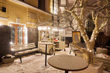 Parkta kış akşamı, karla kaplı banklar, parlak ışıklar beyaz karı aydınlatıyor, yeni yıl arifesinde kar yağıyor..