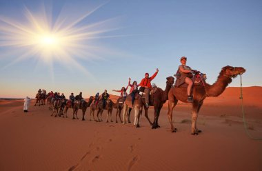 Sahra Çölü 'nün huzurunu yaşayın. Turistler Fas' taki büyüleyici kum tepelerinde keyifli bir deve yürüyüşü yapıyorlar..