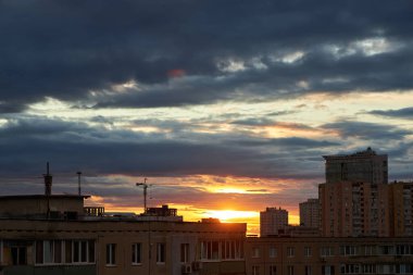 A moody sunset with clouds rolling over a city skyline. The sun peeks through the clouds, casting a warm glow over the buildings, contrasting with the darkening evening sky. clipart