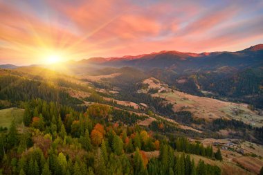 Dağ ormanı, akşam gökyüzü altında güneş ışığında bulutlarla kaplı. Hava aracı görünümü.