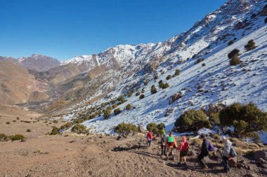 Bir grup turist Fas 'taki büyüleyici Atlas Dağları' nda yürüyüş yaparak engebeli arazinin güzelliğini kucaklıyor ve doğayla iç içe geçiyor.