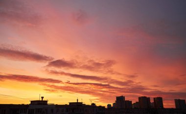 A vibrant sunset paints the sky with warm orange and red hues, contrasting with dark clouds. The city skyline is silhouetted, with a crane and buildings adding an urban touch to the dramatic scene. clipart