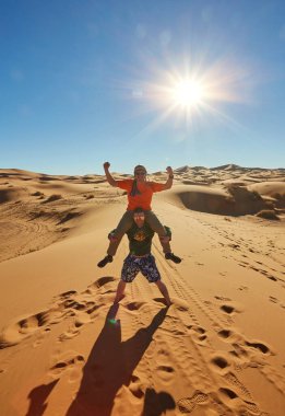 A lively group of tourists captures moments in the Sahara Desert, striking cheerful poses clipart