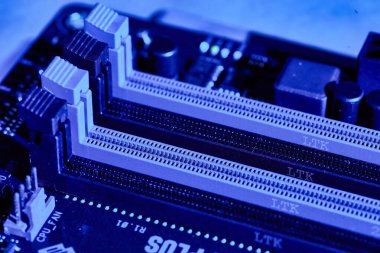 Close-up of RAM slots on a motherboard under blue lighting, showcasing the slots for memory modules and intricate details of the circuit board. Perfect for tech-related content or backgrounds. clipart