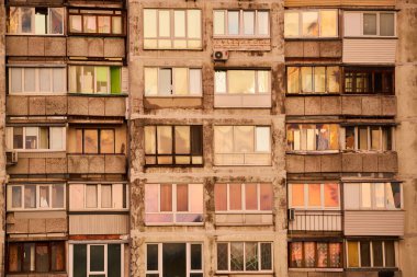 Sovyet tarzı bir apartmanın pencerelerine yakın çekim. Gün batımının ılık renklerini yansıtıyor. Dış görünüş ve çeşitli pencere tasarımları şehir mimarisinin benzersizliğini vurgular..